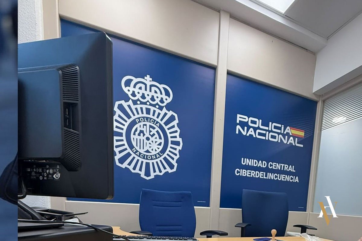 Oficina de la Unidad Central de Ciberdelincuencia de la Policía Nacional de España, con logotipos oficiales en un fondo azul y mobiliario de oficina en primer plano