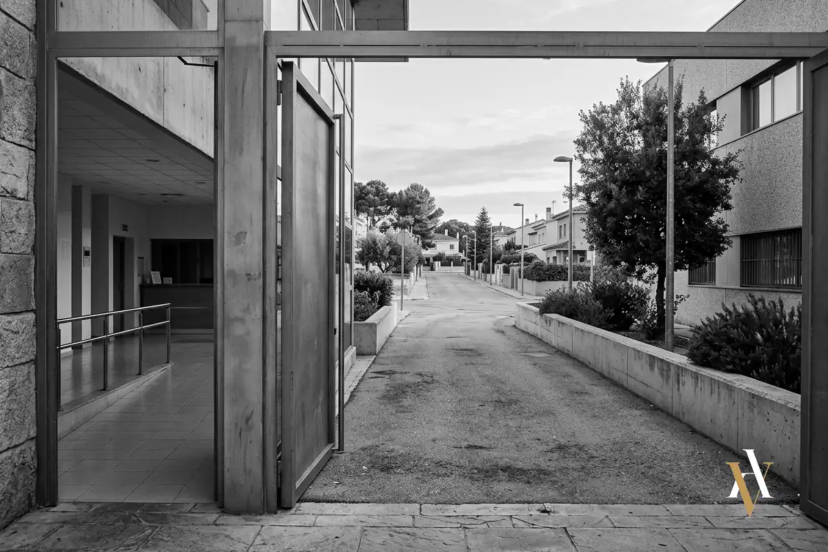Puerta abierta de un Centro de Inserción Social a primera hora de la mañana, con luz natural y un camino de salida hacia la calle